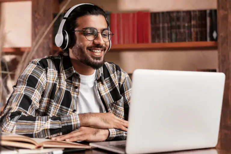 Un étudiant, casque sur les oreilles, travaille sur son ordinateur portable devant une bibliothèque.